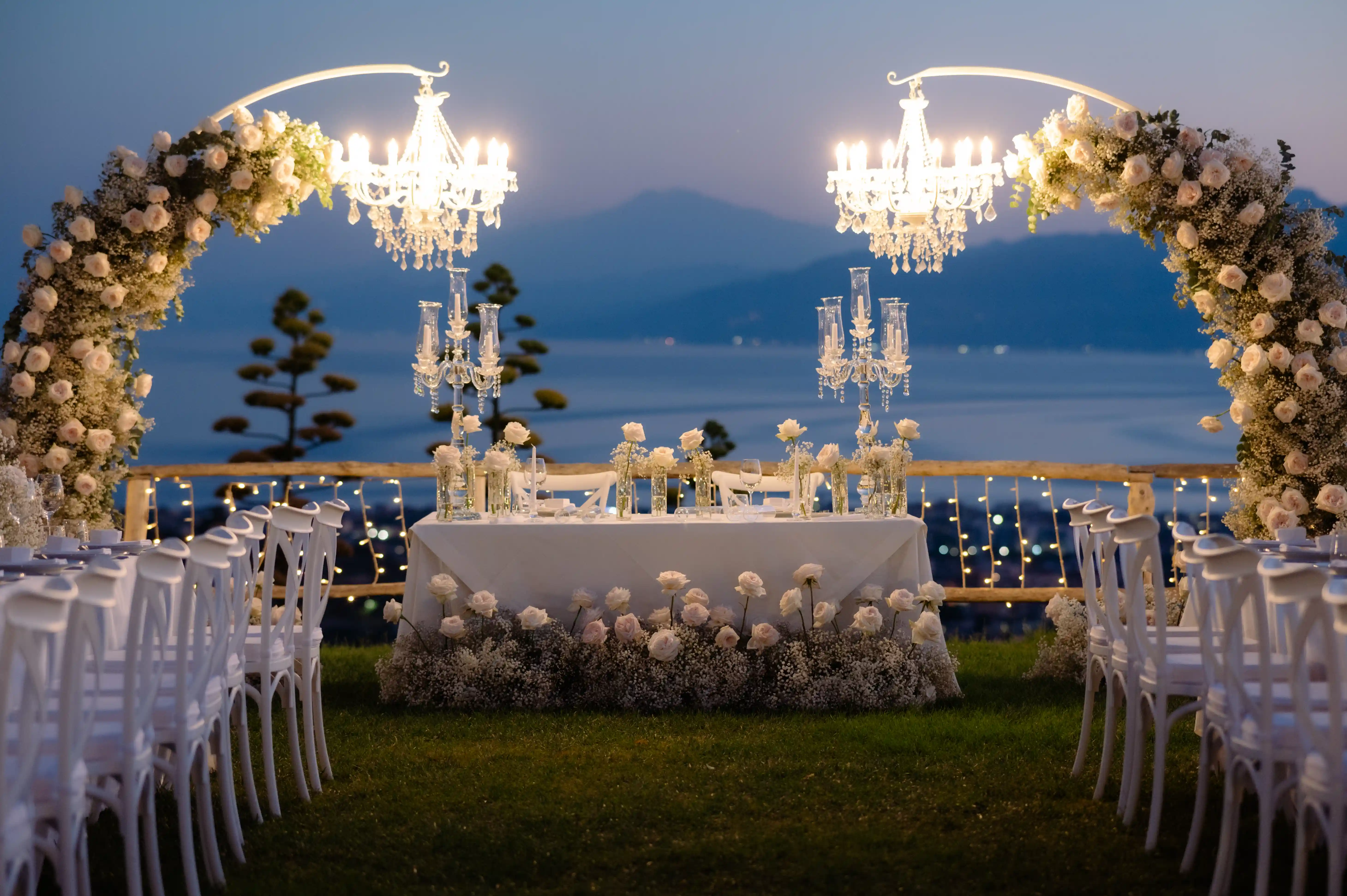 Setup crepuscolare con chandeliers e archi floreali — venue vista mare